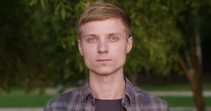Close-up. Portrait of a man in a shirt, blond guy, against a background of green trees, slow motion.