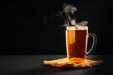 Black hot tea in clear glass Cup, steam coming out of mug on black background