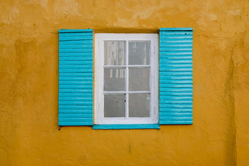 Colorful yellow wall and window with blue shutters