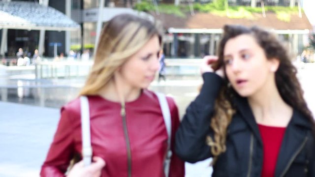 Two female friends walking in a modern city and talking