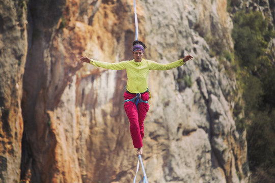 A woman is walking along a stretched sling. Highline in the mountains. Woman catches balance. Performance of a tightrope walker in nature.