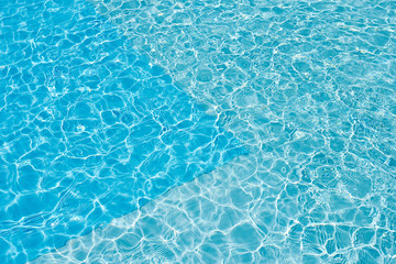Fototapeta na wymiar Background of water in blue swimming pool, water surface with a sun reflection