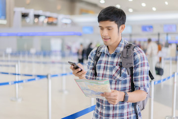 travel vacation concept.Asian man in airport or train station using travel app on a smartphone call someone,Asia male tourist reading map while waiting for taxi or bus with a bag, ready for journey