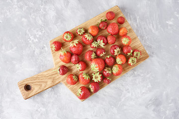 Heap of fresh strawberries with cutting board on a gray background, top view. Healthy nutrition