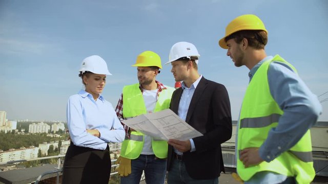 Construction engineer holding architectural plan explaining to workers helmets