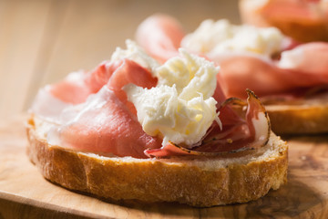 simple bruschetta with prosciutto and mozzarella on wood board