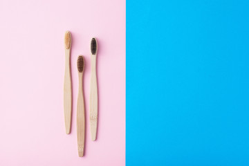 Three natural wooden toothbrushes on a blue and pink color background, flat lay top view. Concept of zero waste and dental care