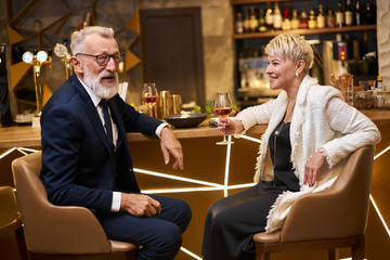 Handsome man in beautiful tuxedo and woman in white blazer sit in expensive beautiful restaurant. Male declare his love. Romantic image, light view