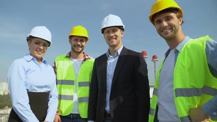 Happy engineers and workers in helmets smiling on camera, construction service