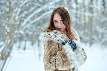 Beautiful young woman in furs on snowy forest background