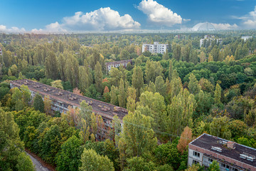 aerial view of the lost city of Pripyat wiht blue sky and clouds. a lot of empty concrete floors overgrown with trees. Pripyat is empty after the evacuation for 33 years after the accident 