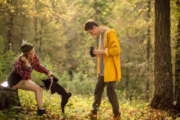 Fototapeta premium cheerful girl in shorts, shirt and hat teaching her pet perform tasks while her boyfriend taking photos, entertainment, happiness