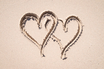 Bright sunny view of pair of hearts intertwined in smooth sand in a symbol of love and tropical travel on an empty beach