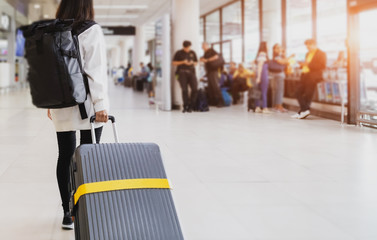 Young woman pulling suitcase in airport terminal. Young woman traveler in international airport with backpack holding suitcase or baggage in her hand, Beautiful young tourist girl with backpack 