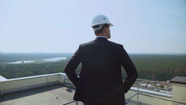 Male architect in helmet standing roof looking around, construction supervisor