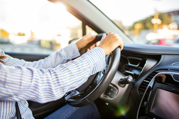 Female hands on the steering wheel of a car while driving. Sunset the background, the windshield and road. Woman driving a car. Hands on wheel driving car in city