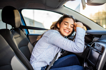 Young and cheerful woman enjoying new car hugging steering wheel sitting inside. Woman driving a...