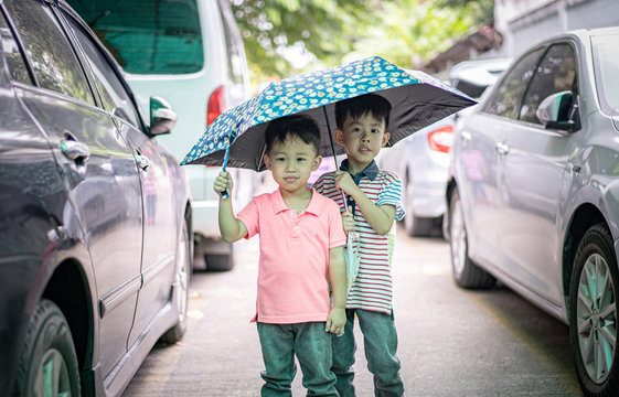 2 brothers are walking together on the street with an umbrella in the rain.