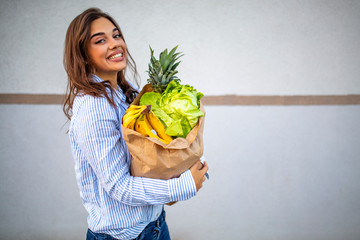 Close up portrait of a happy pretty girl holding bag with groceries and looking at camera with copy space. Close up of a woman holding heavy bag with groceries. Carrying a healthy bag
