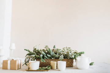 Festive Christmas, New Year composition with fir-tree branches, gift box, decorations, mug, kettle and candle in modern interior. Winter holidays minimal background.