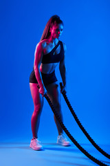 slim well-built sportswoman with ponytail holding ropes, going to train with them, full length side eview photo