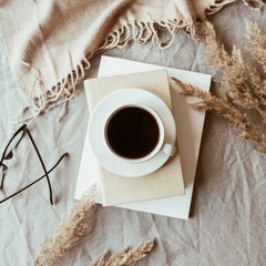 Autumn, fall composition. A cup of coffee lying on the grey linen bed with beige warm blanket, books, glasses and reeds. Lifestyle, hygge concept. Flat lay, top view.