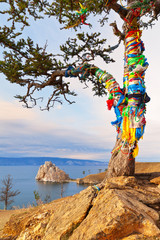 Baikal Lake. Traditions of tourists coming to Olkhon Island to tie colored ribbons on a lone larch on a high hill called the Wish Tree. Shamanka Rock or Cape Burhan in the distance