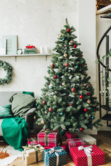 Christmas / New Year composition. Winter holidays concept. Beautiful scandinavian living room decorated with festive christmas fir tree with red, gold and green toys and big gift boxes.