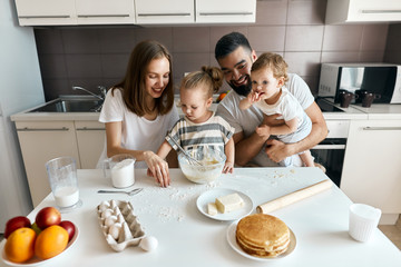 funny family with dirty faces picking flour which is luing on the table, close up photo. family cleaning the messy table in the kitchen