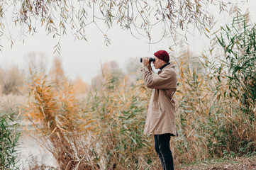 Explorer in forest near lake looks horizon with binoculars