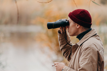 Explorer in forest near lake looks horizon with binoculars
