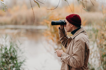 Explorer in forest near lake looks horizon with binoculars