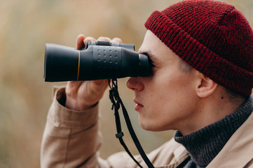 Tracking fauna. Explorer in forest near lake looks horizon with binoculars