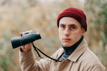 Explorer looking in camera and standing in forest near lake looks horizon with binoculars