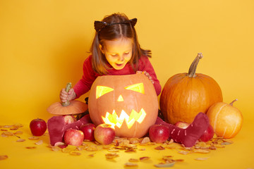 Indoor shot of little cute baby sitting isolated over yellow studio background, Halloween fall...