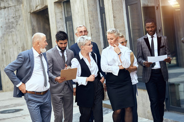 Group of businessmen wear stylish different suits discuss project walking down the street.