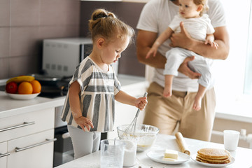 little blonde girl working with whisk while standing on the chair. close up side view photo