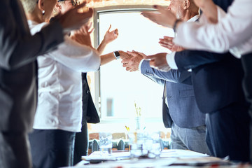 Group of businessmen at table in office. Focuced on shaking hands caucasian man and woman