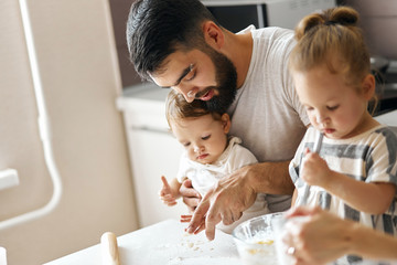 bearded father and his two daughters playing with flour while sitting at the table. close up side...