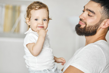 young positive bearded man holding baby in his hands, looking at her with tender expression. close up photo. happy parenthood. close up portrait