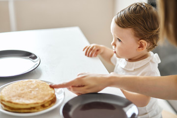 woman pointing to pancakes, asking the kid to taste them. close up cropped side view photo