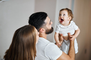 young couple looking at the baby with wide open mouth, checking her new tooth. close up back view photo