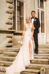 Groom and bride stand on stairs. Fashion model in elegant clothes. White long dress and stylish suit