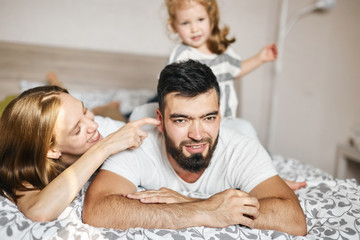 cheerful bearded man lying on the bed, blonde woman touching her husband's ear. close up photo