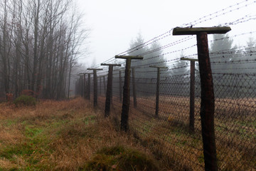 Barbwire fence. Part of the czech german borderline in the middle of a foest on a grey and foggy autumn morning. Trail leading towards an old rotten military boarder watchtower