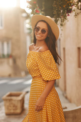 Summer outdoor portrait of young beautiful woman in yellow polka dot dress and thatch hat posing at...