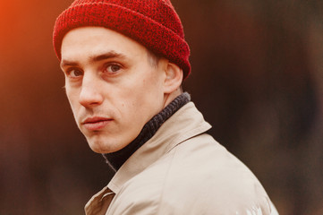 A close-up portrait of a tourist guy. A traveler in a red knitted hat turns back.