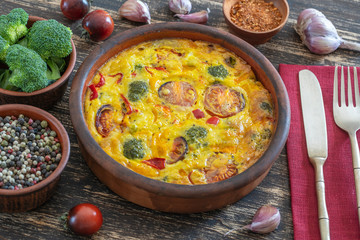 Ceramic bowl with vegetable frittata, simple vegetarian food. Frittata with egg, tomato, pepper, onion, broccoli and cheese on wooden table. Italian egg omelette