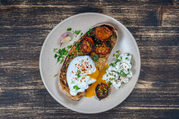 Poached egg on a piece of bread with fried red tomato, garlic and cottage cheese on a plate, close up