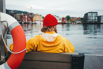 Back view of male tourist wearing yellow jacket sitting on bench in front of city pier. Man tourist...
